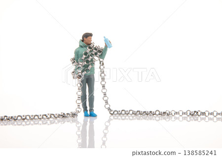 Miniature person holding a water bottle while tangled in a chain on a plain background Miniature person holding a water bottle while tangled in a chain on a plain background 138585241