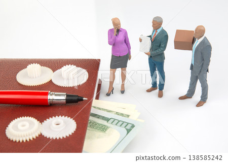 Miniature people discuss items on a table with gears, money, and a pen during a business meeting Miniature people discuss items on a table with gears, money, and a pen during a business meeting 138585242