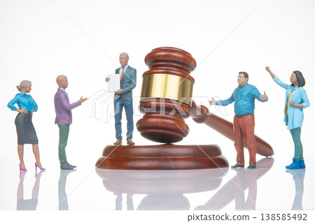 Miniature figures engage in a legal discussion beside a large wooden gavel in a simple setup indoors 138585492
