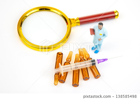 A researcher in a lab coat looks at vials and a syringe with a magnifying glass A researcher in a lab coat looks at vials and a syringe with a magnifying glass 138585498