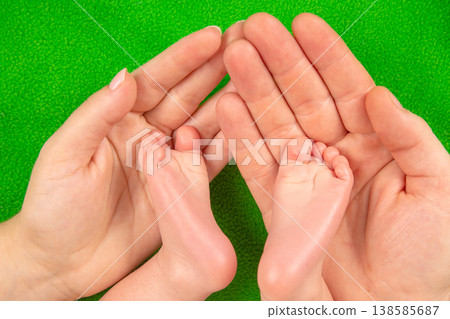 Hands holding small baby feet against a bright green background during a family moment  138585687