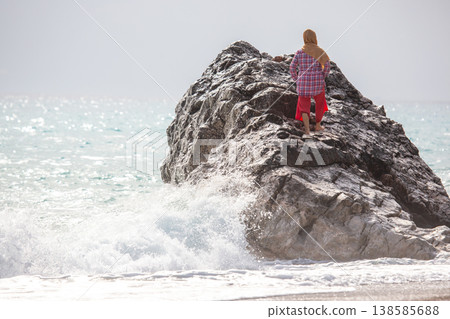 Woman stands on a rock by the sea looking at waves and the horizon in the early morning light Woman stands on a rock by the sea looking at waves and the horizon in the early morning light 138585688