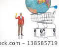 Miniature person holding trophy stands near a shopping cart with a globe in a bright studio setting 138585719