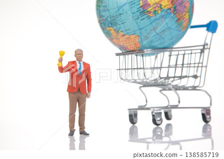 Miniature person holding trophy stands near a shopping cart with a globe in a bright studio setting 138585719