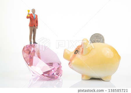 Miniature people stand on a crystal holding a trophy, while a piggy bank waits with a coin resting Miniature people stand on a crystal holding a trophy, while a piggy bank waits with a coin resting 138585721