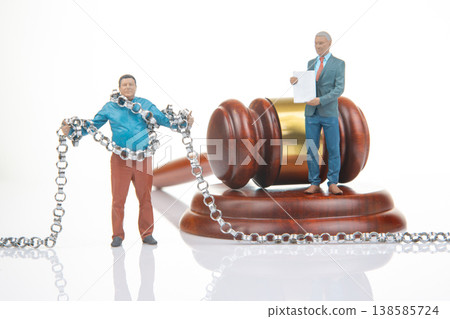 Miniature people with chain near a gavel and a man holding a document in a studio setting during Miniature people with chain near a gavel and a man holding a document in a studio setting during 138585724