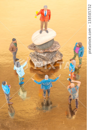 Miniature people gather around a figurine on a stone during a colorful scene at sunset 138585732
