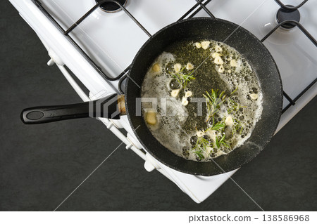 Cooking herbs and garlic in a pan on a stove in a kitchen during the day Cooking herbs and garlic in a pan on a stove in a kitchen during the day 138586968