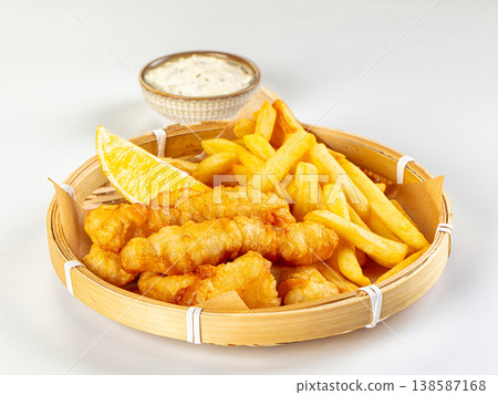 Classic fish and chips served in a basket with lemon and tartar sauce, isolated on white background Classic fish and chips served in a basket with lemon and tartar sauce, isolated on white background 138587168