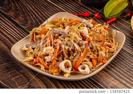 Stir-fried seafood noodles with shrimp and squid in a bowl on a wooden table. Stir-fried seafood noodles with shrimp and squid in a bowl on a wooden table. 138587425