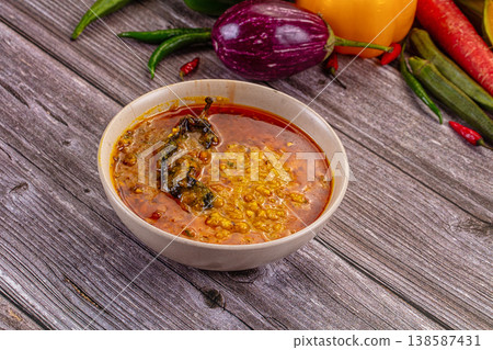 Spicy Indian lentil curry, dal tadka, in a bowl on a wooden background with fresh ingredients. Spicy Indian lentil curry, dal tadka, in a bowl on a wooden background with fresh ingredients. 138587431