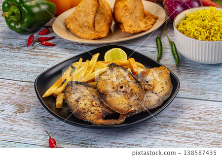 Fried fish steaks with french fries, lemon, and side dishes on a rustic blue wooden table 138587435