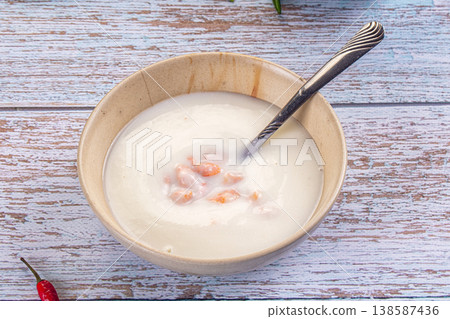 Bowl of creamy shrimp soup with a spoon on a rustic light blue wooden table with fresh chili peppers. Bowl of creamy shrimp soup with a spoon on a rustic light blue wooden table with fresh chili peppers. 138587436