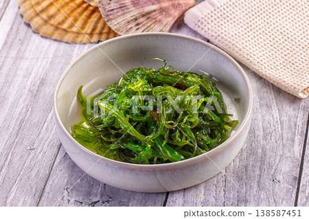 Japanese seaweed salad Chuka with sesame seeds and chili in a white bowl on a wooden table. 138587451