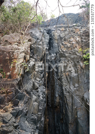 A steep, dark, and rugged rock face in Vietnam with a rope descending, hinting at adventure or a challenging climb A steep, dark, and rugged rock face in Vietnam with a rope descending, hinting at adventure or a challenging climb 138587779