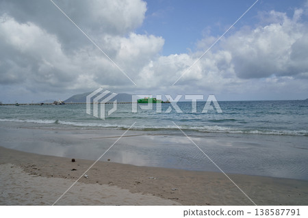 A serene beach scene in Vietnam with gentle waves lapping the shore and a distant pier with a green ferry A serene beach scene in Vietnam with gentle waves lapping the shore and a distant pier with a green ferry 138587791