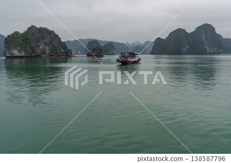 A tourist boat navigates through the iconic limestone karsts of Ha Long Bay under an overcast sky 138587796