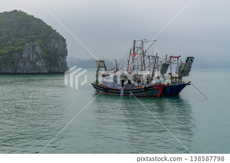 Two traditional Vietnamese fishing vessels are anchored in the calm waters of Ha Long Bay amidst a misty morning 138587798