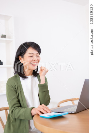 A housewife in her 50s makes a triumphant gesture while doing calculations. A housewife in her 50s makes a triumphant gesture while doing calculations. 138589129