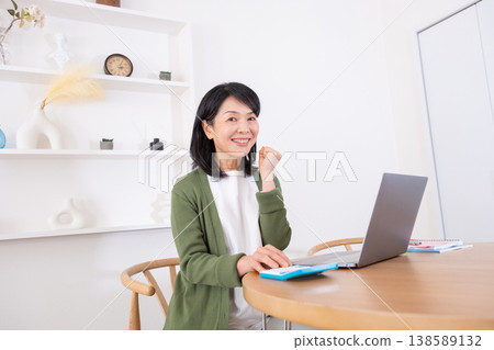 一位五十多歲的家庭主婦在使用計算器時做出了一個得意的手勢。 一位五十多歲的家庭主婦在使用計算器時做出了一個得意的手勢。 138589132
