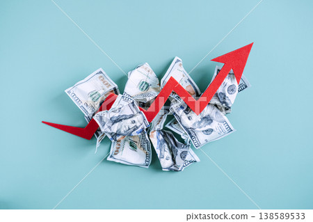 Red arrow rises above pile of crumpled banknotes on blue background. Cost of living crisis, wealth erosion factors, interest rate hike. Red arrow rises above pile of crumpled banknotes on blue background. Cost of living crisis, wealth erosion factors, interest rate hike. 138589533