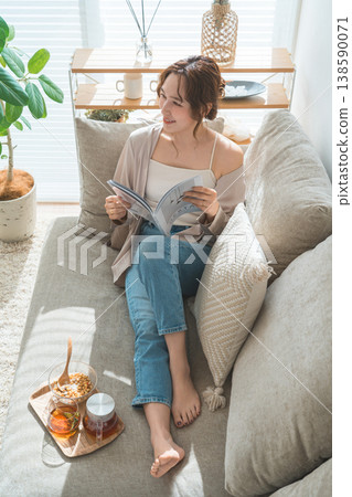A stylish Asian woman sitting on the sofa in the living room and reading a magazine during tea time A stylish Asian woman sitting on the sofa in the living room and reading a magazine during tea time 138590071