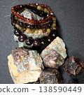 Handcrafted almandine garnet bracelets and raw mineral specimens resting on dark surface. Polished gemstone beads and natural rough stones 138590449