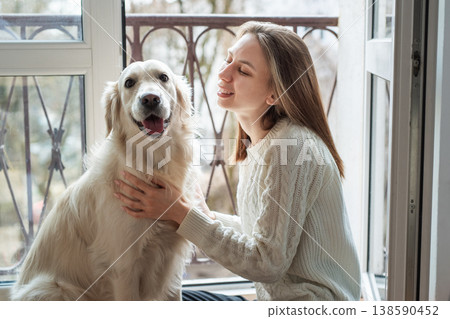 Woman petting golden retriever dog by window Woman petting golden retriever dog by window 138590452
