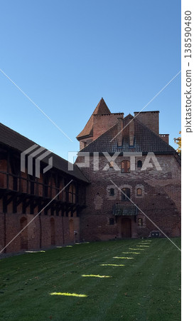 Malbork Castle courtyard with red brick building wooden gallery and grass lawn with sunlight and shadow under clear sky. Architecture, history and travel concept 138590480