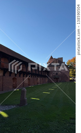 Inner courtyard of Malbork Castle in Poland with red brick buildings wooden gallery and green lawn under clear blue sky. Architecture, history and travel concept Inner courtyard of Malbork Castle in Poland with red brick buildings wooden gallery and green lawn under clear blue sky. Architecture, history and travel concept 138590504