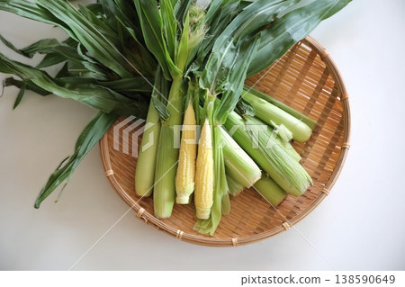 Young corn with the husks on, placed on a bamboo sieve Young corn with the husks on, placed on a bamboo sieve 138590649