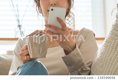 Asian woman sitting on the sofa in the living room and looking at her smartphone Asian woman sitting on the sofa in the living room and looking at her smartphone 138590698
