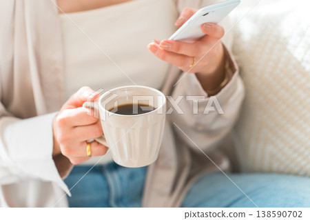 A woman's hands as she sits on the living room sofa and looks at her smartphone. A woman's hands as she sits on the living room sofa and looks at her smartphone. 138590702