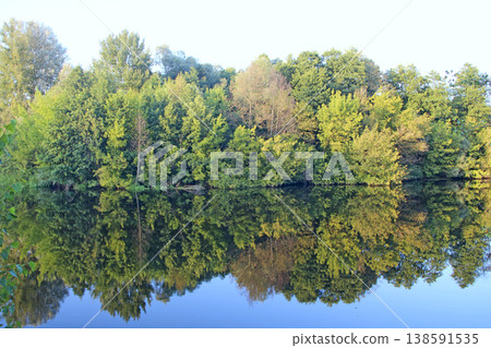 Landscape with trees reflected on water surface of river Landscape with trees reflected on water surface of river 138591535