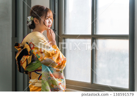 A 20-year-old woman in a furisode kimono gazes out the window of a retro, antique Western-style mansion/studio. A 20-year-old woman in a furisode kimono gazes out the window of a retro, antique Western-style mansion/studio. 138591579