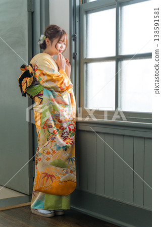 A 20-year-old woman in a furisode kimono gazes out the window of a retro, antique Western-style mansion/studio. A 20-year-old woman in a furisode kimono gazes out the window of a retro, antique Western-style mansion/studio. 138591581