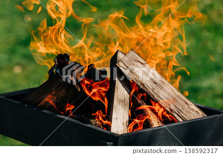 Birch logs burning in a grill on spring holiday, green grass, festive season Birch logs burning in a grill on spring holiday, green grass, festive season 138592317