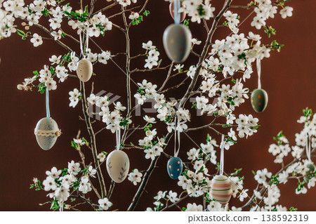 Decorative Easter eggs hanging on a string from a flowering cherry blossom branch indoors Decorative Easter eggs hanging on a string from a flowering cherry blossom branch indoors 138592319