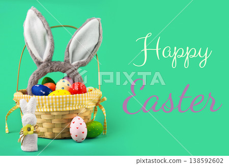 Easter basket with colorful painted eggs, fluffy bunny ears, and a white toy bunny on a bright green background with Happy Easter text. Perfect for spring holiday greetings. High quality photo 138592602