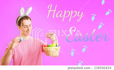 Cheerful man in bunny ears holding a blue Easter egg and a basket full of colorful eggs against a pink background with Happy Easter text and paw prints. Festive spring concept. High quality photo Cheerful man in bunny ears holding a blue Easter egg and a basket full of colorful eggs against a pink background with Happy Easter text and paw prints. Festive spring concept. High quality photo 138592814