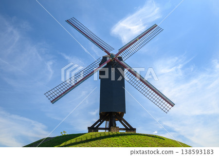 Traditional windmill on grassy hill under blue sky Traditional windmill on grassy hill under blue sky 138593183