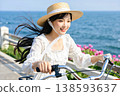 一位年輕女子騎著自行車穿過沿海的花田。 138593637