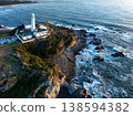 日出時的燈塔和拍打著海岸的白色浪花。 138594382