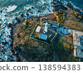 日出時的燈塔和拍打著海岸的白色浪花。 138594383