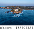 日出時的燈塔和拍打著海岸的白色浪花。 138594384