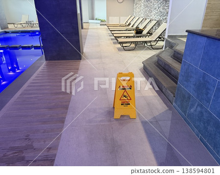 Caution wet floor sign in spa area with lounge chairs, swimming pool, and modern interior design Caution wet floor sign in spa area with lounge chairs, swimming pool, and modern interior design 138594801