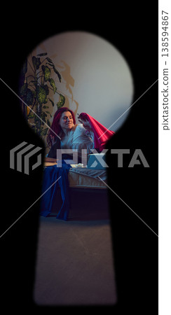 Woman smiling while looking through red clothing on bed seen through keyhole Woman smiling while looking through red clothing on bed seen through keyhole 138594867