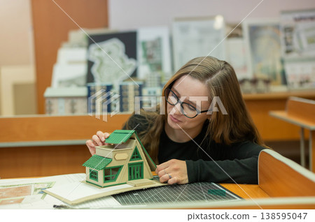 Caucasian young woman making a model of a building. Student of the construction university. Caucasian young woman making a model of a building. Student of the construction university. 138595047