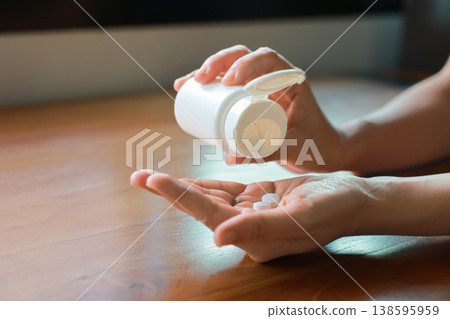 Close up of person hands pouring white pills from a white plastic bottle into their palm. Taking daily medicine, vitamin, painkiller or dietary supplement for healthcare medical treatment concept. Close up of person hands pouring white pills from a white plastic bottle into their palm. Taking daily medicine, vitamin, painkiller or dietary supplement for healthcare medical treatment concept. 138595959