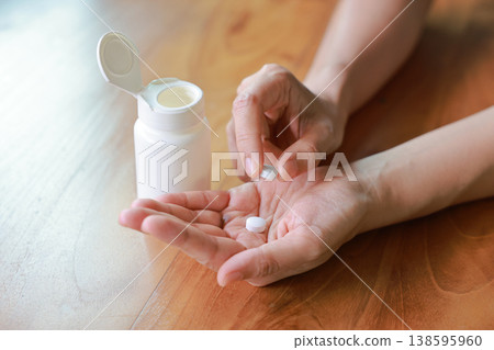 Close up of person hands pouring white pills from a white plastic bottle into their palm. Taking daily medicine, vitamin, painkiller or dietary supplement for healthcare medical treatment concept. Close up of person hands pouring white pills from a white plastic bottle into their palm. Taking daily medicine, vitamin, painkiller or dietary supplement for healthcare medical treatment concept. 138595960
